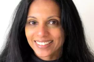 Dr Seema Vyas with long dark hair smiling, wearing a black turtleneck against a plain background.