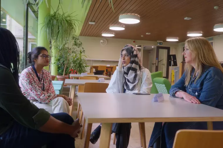 Still from film, 4 people sit around a table talking